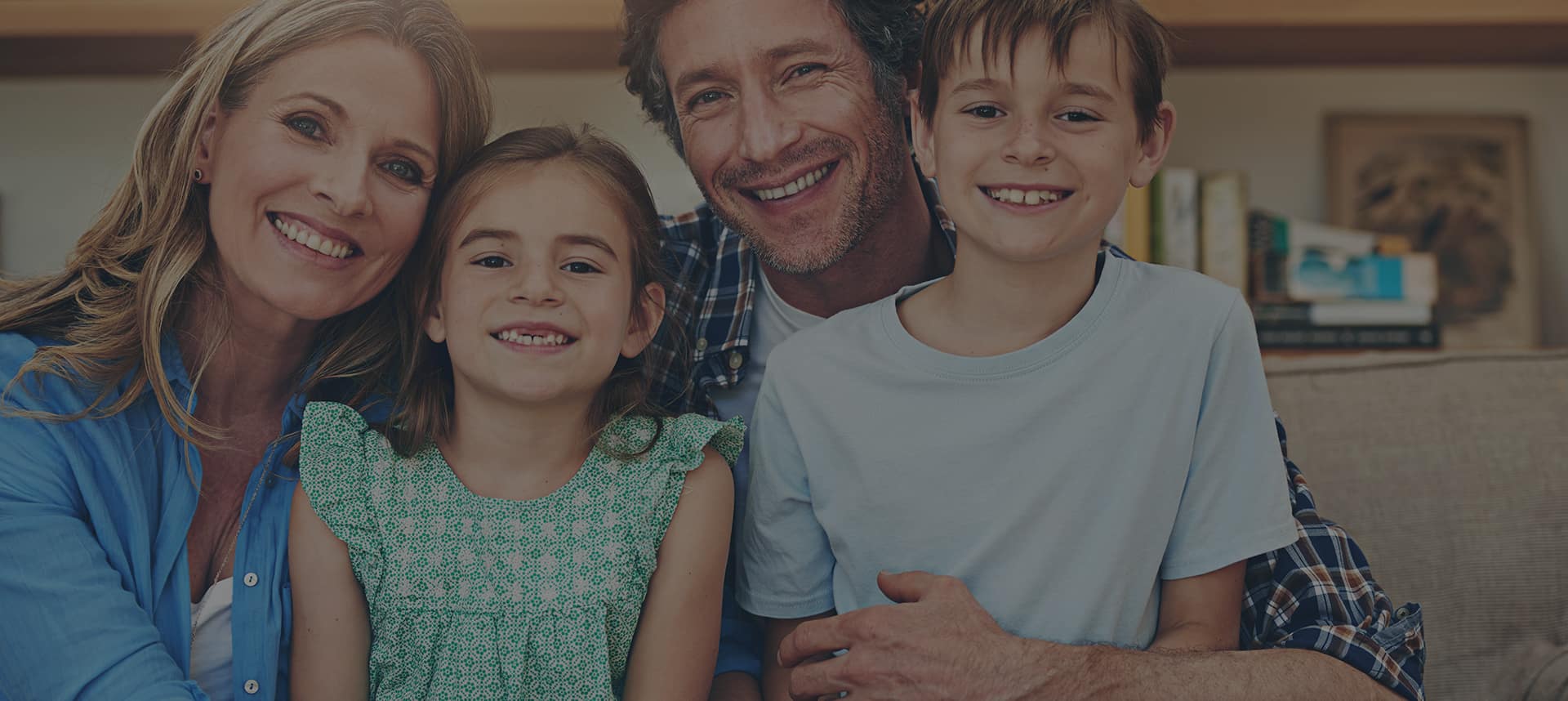 Smiling family of four, including a mother, father, daughter, and son, sitting together in a cozy living room, representing family therapy and support for family-related issues.